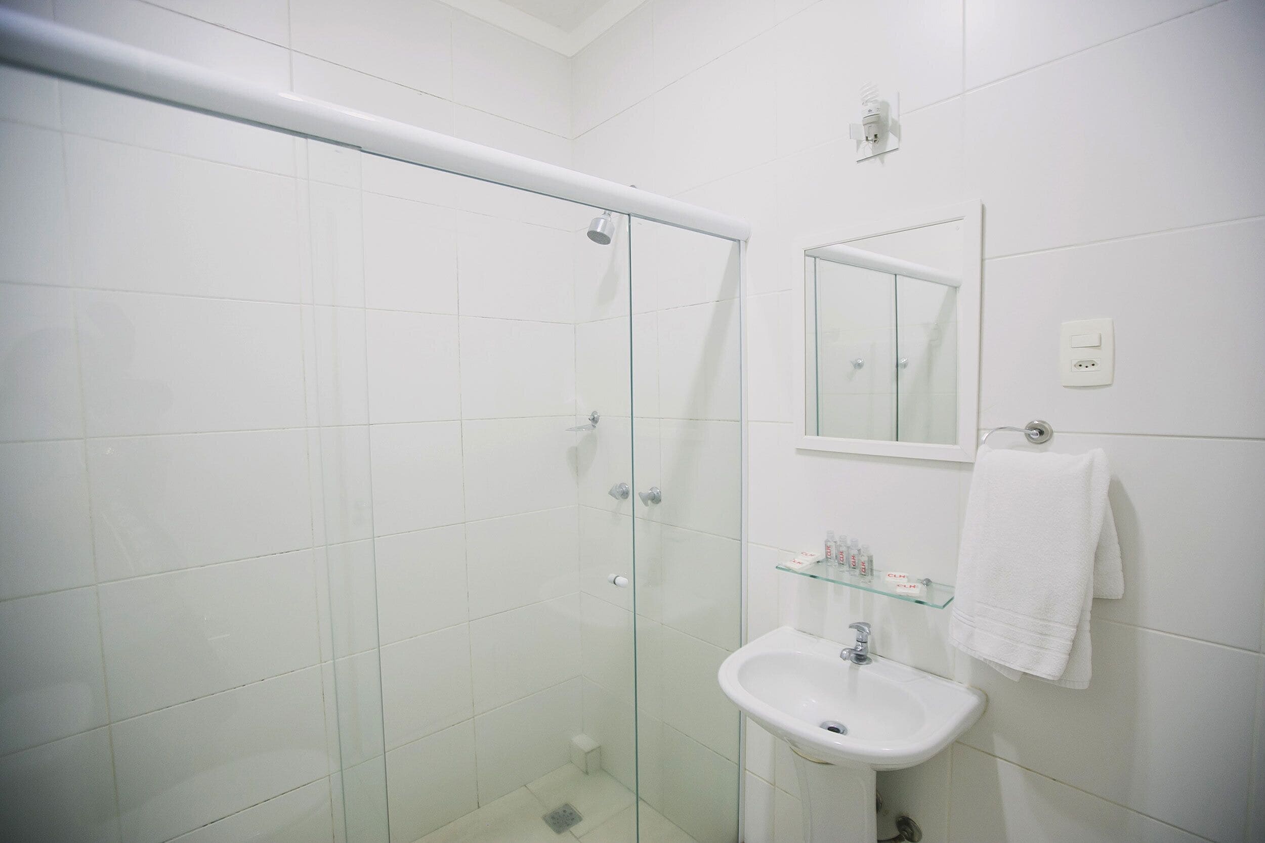 Een badkamer met een douchecabine van glas, een wit wastafelmeubel, een spiegel en een handdoekrek.