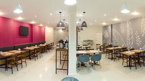 Un espace de restauration moderne avec des banquettes et des tables, une cuisine en arrière-plan et un mur décoratif orné de motifs de feuilles.
