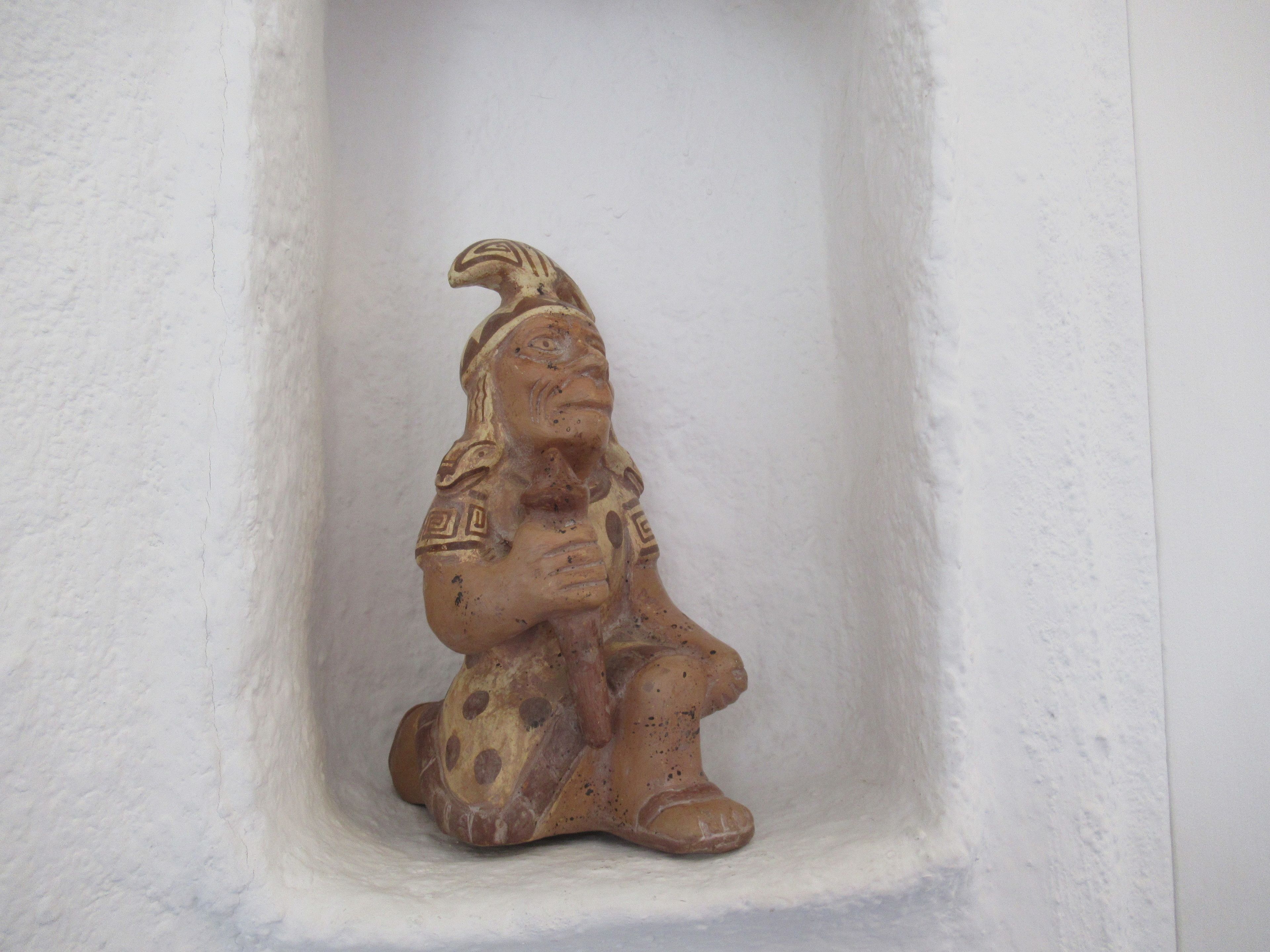 A small, ancient-looking statue with intricate carvings, placed in a niche against a plain wall.