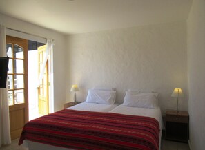 Un dormitorio con una cama, dos lámparas de noche, un ventanal con cortinas y una puerta de madera.