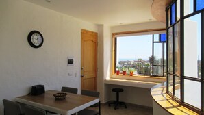 Een eetruimte met een houten tafel, stoelen, een klok en een raam met uitzicht op zee.
