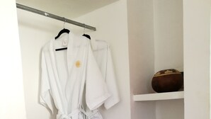 A bathroom with a towel rack holding two white robes, a shelf with a bowl, and a shelf with toilet paper.