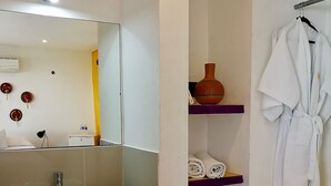A bathroom with a white sink, a mirror, a towel rack, and a shelf with toiletries.
