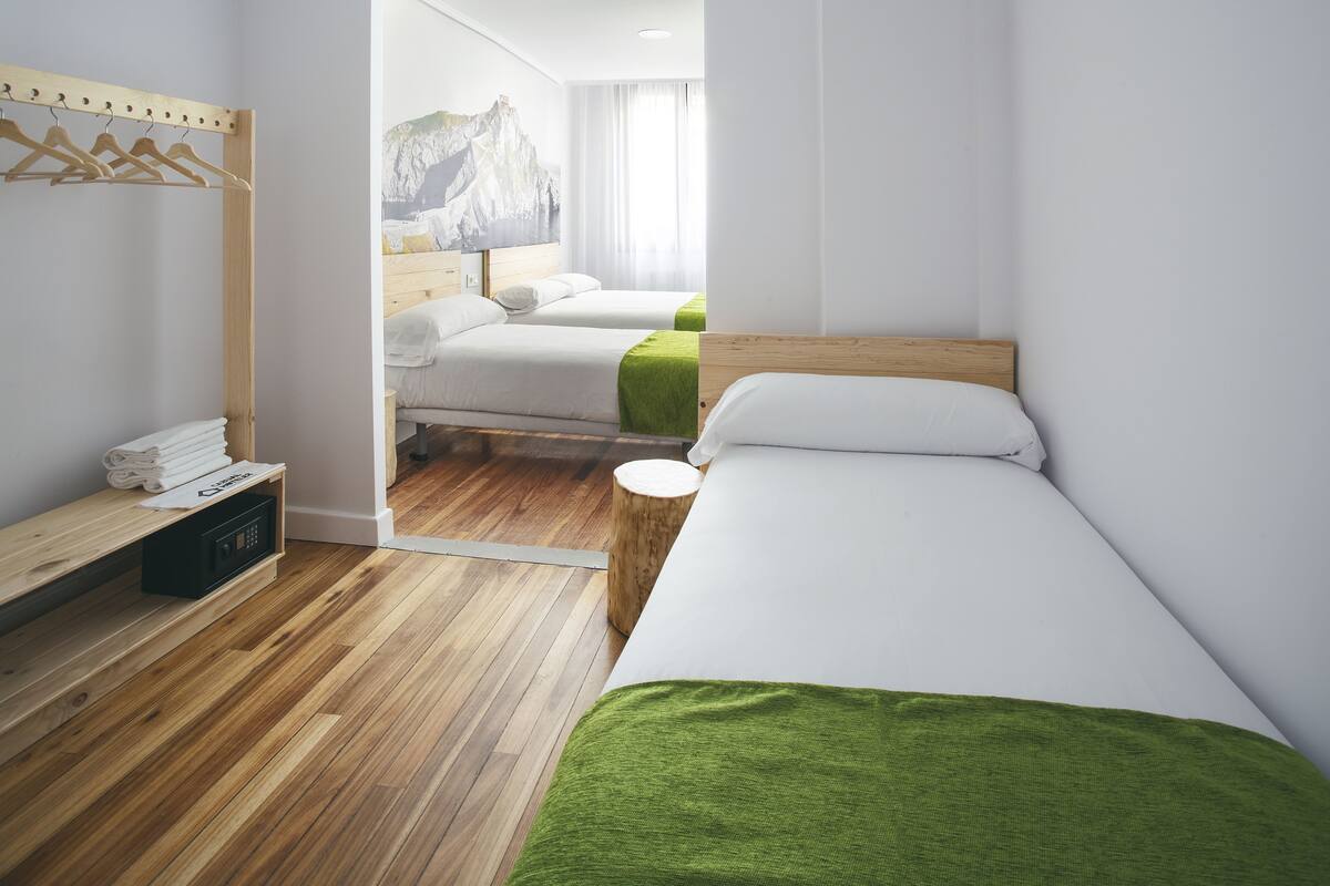 Habitación de hotel con dos camas, suelo de madera, cabecero de madera, un taburete de madera pequeño y un perchero de toallas fijado a la pared.