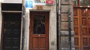 Un edificio con puerta de madera numerada con el 14, un letrero azul que dice 'CAJUAL SERANTES' y un letrero rojo de 'segurima', además de un cartel de estacionamiento visible.