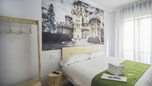 Habitación de hotel con una cama, una mesita de noche de madera, un perchero para toallas en la pared, un control remoto y un cuadro con temática de castillo.