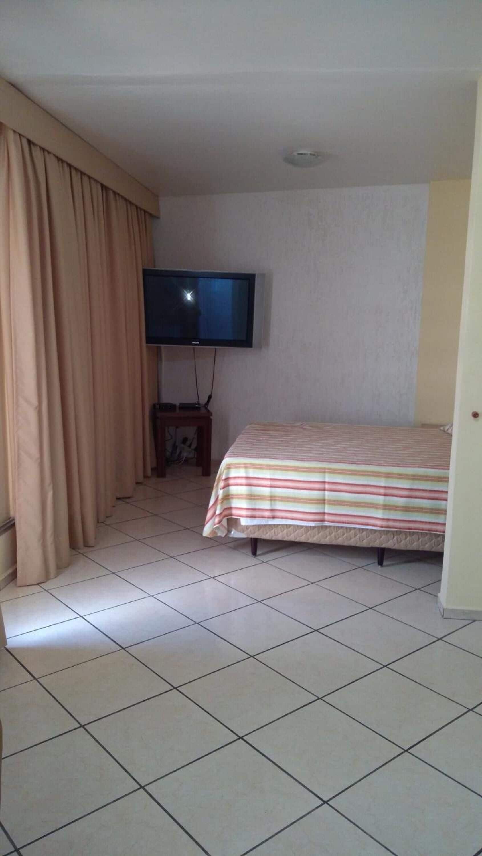 Une chambre avec un lit, un téléviseur fixé au mur et un rideau.