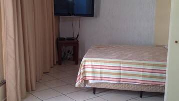 Une chambre avec un lit, un téléviseur fixé au mur et un rideau.
