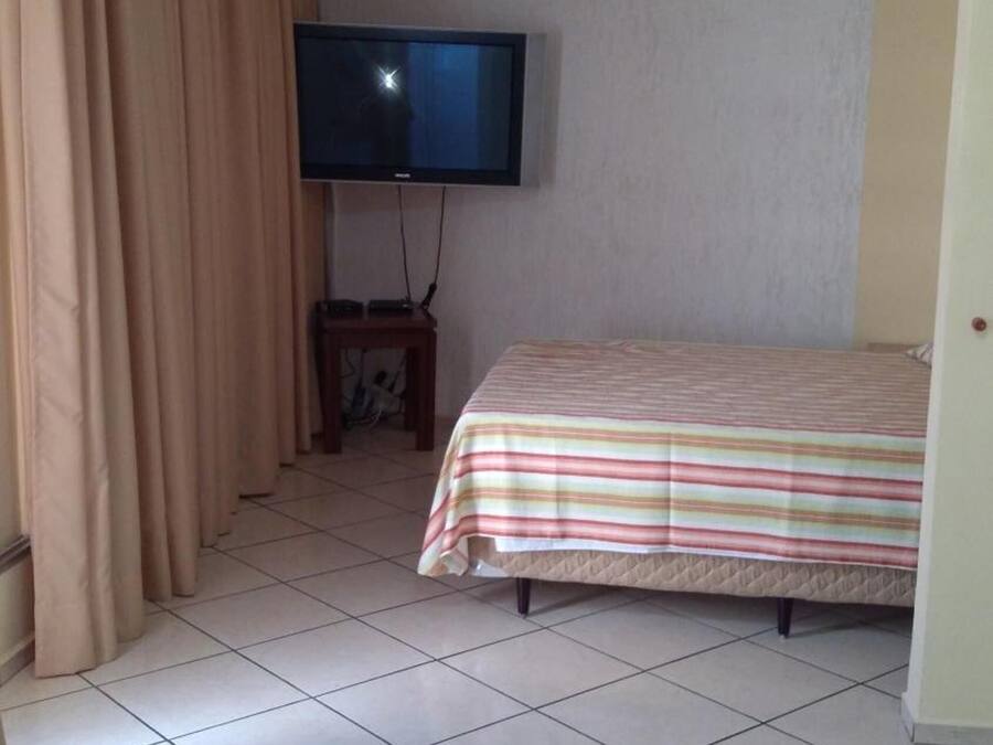Une chambre avec un lit, un téléviseur fixé au mur et un rideau.
