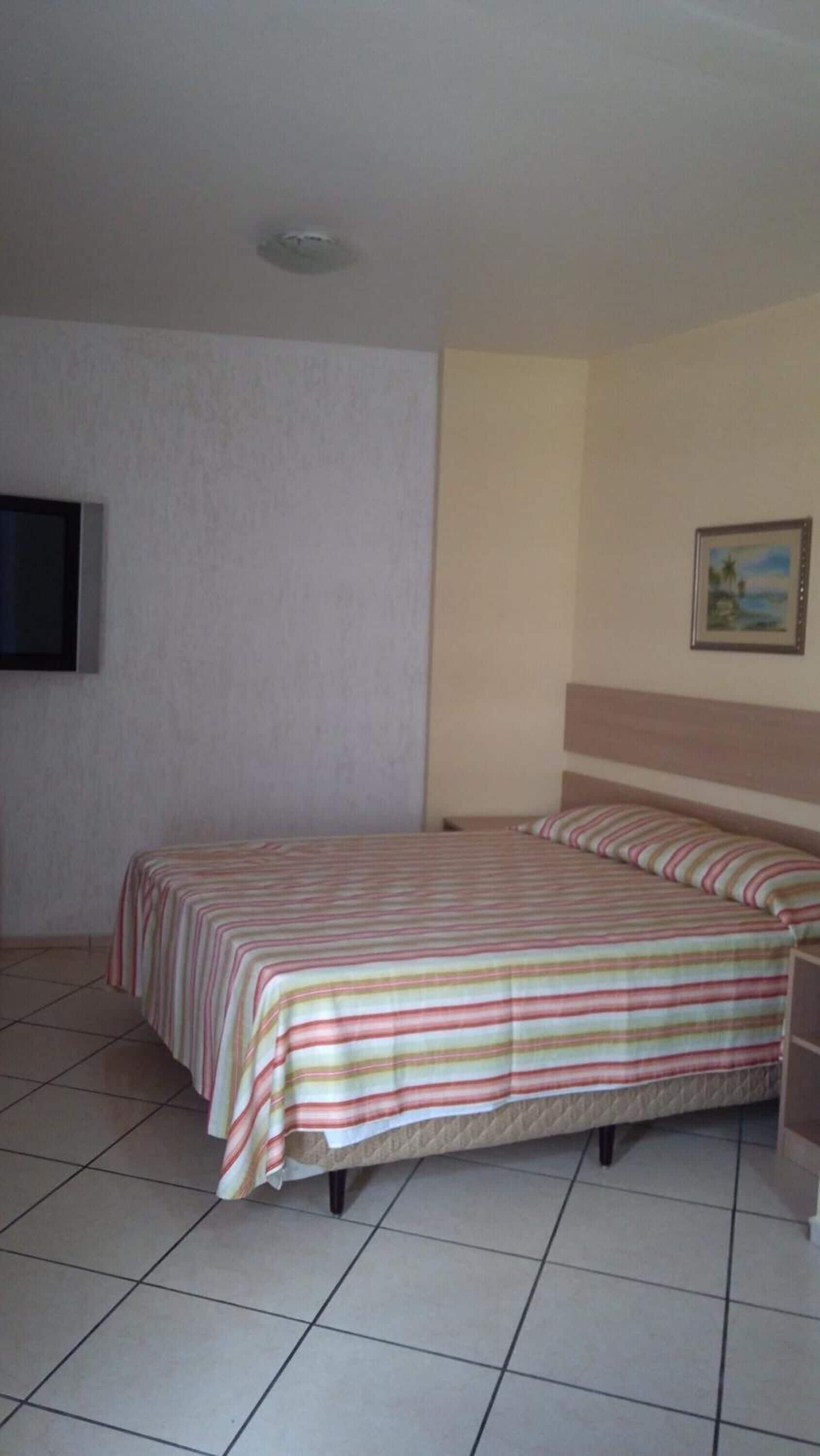 Una camera d'albergo con un letto, una televisione a parete e un quadro appeso.