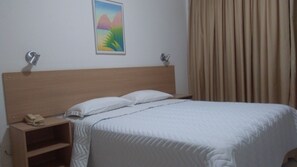 A hotel room with a wooden headboard, a bed with white bedding, a bedside table with a telephone, and a painting on the wall. - Hotel Ipanema Inn (São Paulo)
