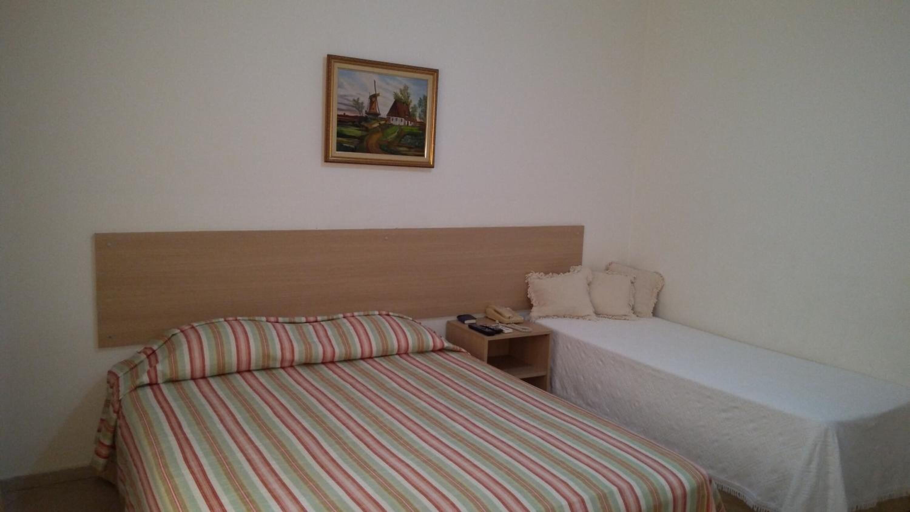 A single room with a bed, a nightstand, a telephone, and a painting on the wall.