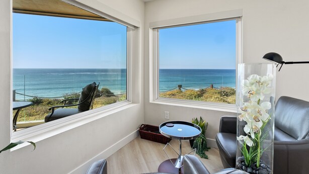 A modern room with large windows overlooking the sea, a round table, and a chair.