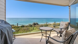 A balcony with a view of the ocean, a table, and a chair.