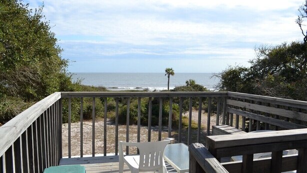 Une terrasse en bois avec une table et des chaises, donnant sur une plage et l’océan.