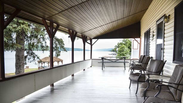 A covered porch with a table and chairs, overlooking a lake.
