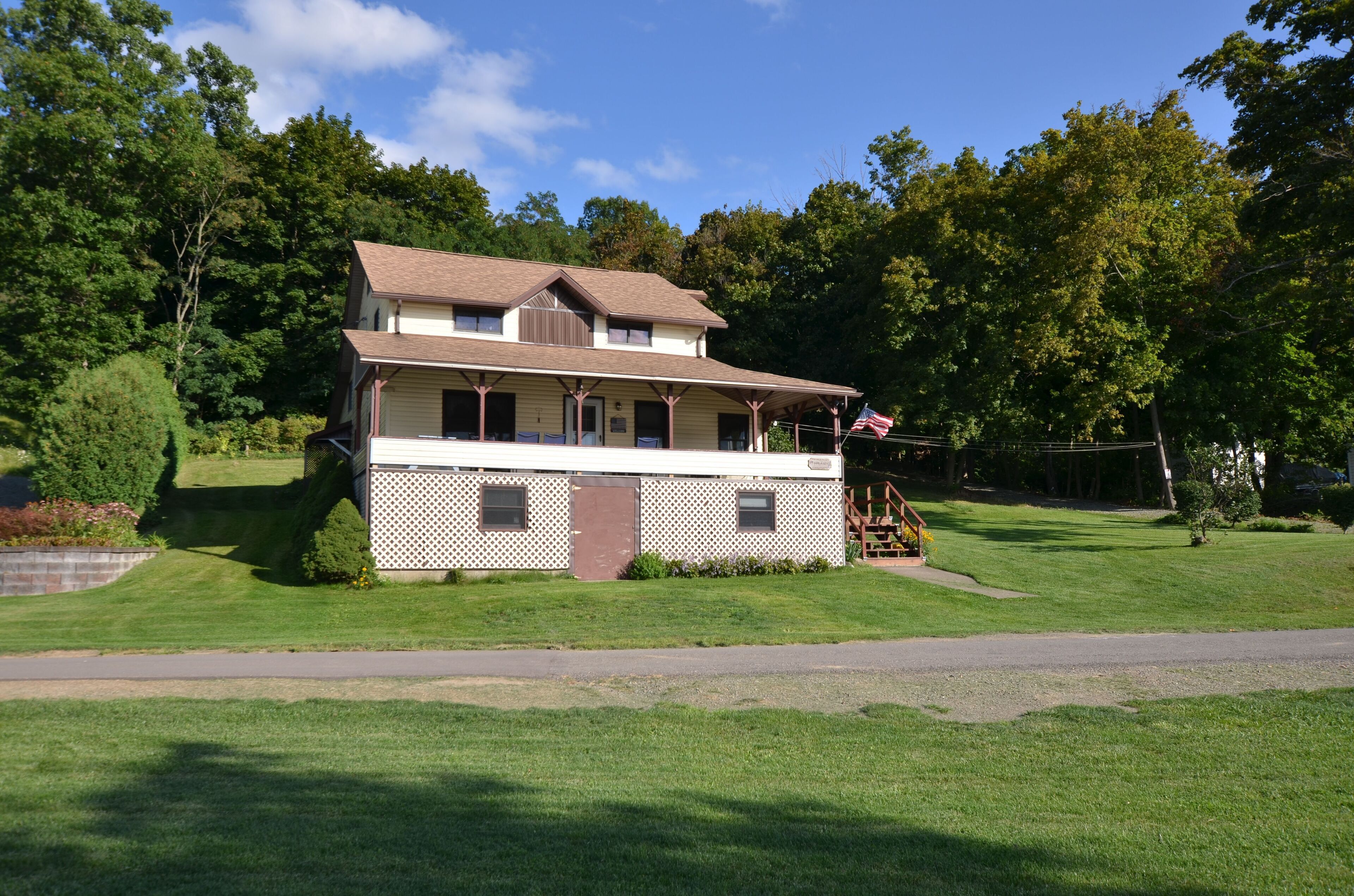 A two-story house with a porch and a small deck, surrounded by a well-maintained lawn and trees.