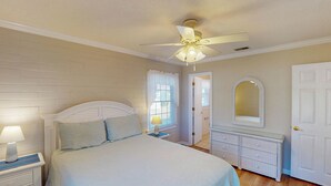 A bedroom with a bed, nightstand, lamp, dresser, mirror, ceiling fan, and a door.