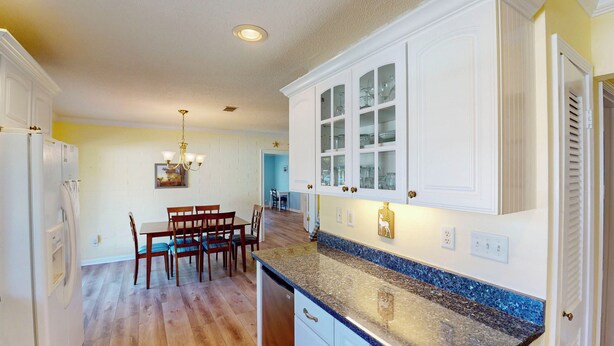 A kitchen with white cabinets, a granite countertop, and a dining area with wooden chairs and a table.