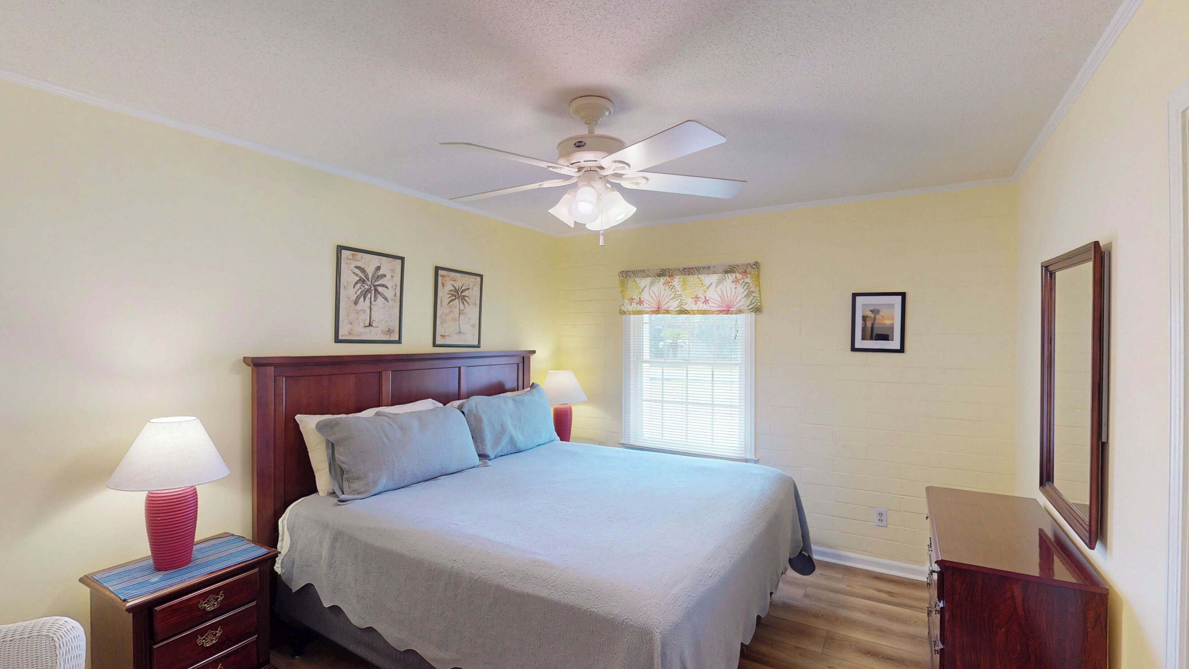 A bedroom with a bed, nightstands, a ceiling fan, and framed pictures on the wall.