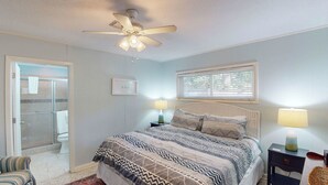 Ein Schlafzimmer mit einem Bett, zwei Nachttischlampen, einem Deckenventilator, einem Fenster mit Jalousien und einer Tür zum Badezimmer.