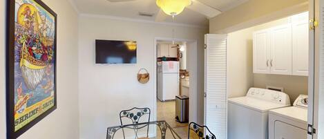 A compact kitchen with a ceiling fan, a refrigerator, a washing machine, and a dining area with a table and chairs.