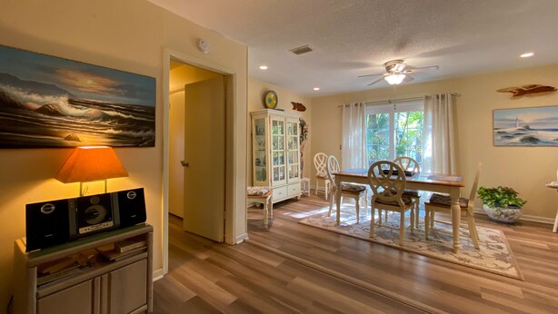 A dining area with a wooden table and chairs, a ceiling fan, and a view of the outdoors through a window. - Island Pines 3 bedrooms, 2 bathrooms (Jekyll Island)