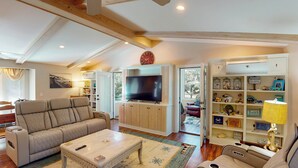 A living room with a beige sofa, a coffee table, a flat-screen TV, and a bookshelf with decorative items.