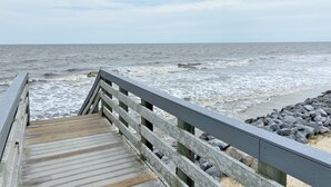 A wooden boardwalk leading to a rocky beach with the ocean in the background.