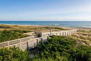 Ein hölzerner Steg führt zu einem Strand mit freiem Blick auf das Meer und den entfernten Stadtgürtel.