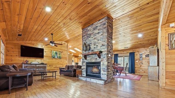 A spacious living room with a stone fireplace, wooden ceiling, and a flat-screen TV mounted on the wall.