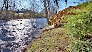 A river with a wooden staircase leading down to it, surrounded by trees and grass.