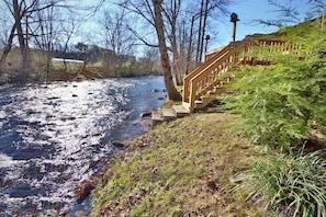 Un río con una escalera de madera que baja hasta sus orillas, rodeado de árboles y hierba.