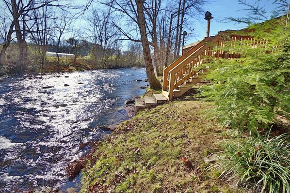 A river with a wooden staircase leading down to it, surrounded by trees and grass.