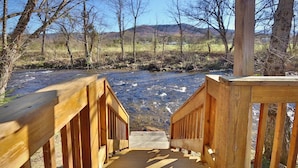 A wooden staircase leading down to a river, surrounded by trees and a mountain in the background.