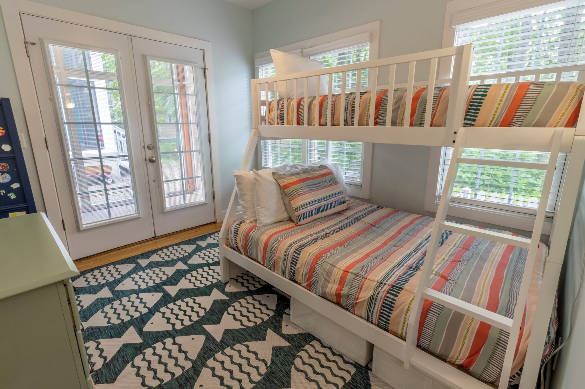 Una cama individual con ropa de cama a rayas, un tapete con diseño geométrico y una puerta que da a vistas del exterior.