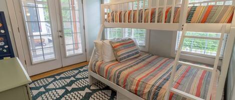 Una cama individual con ropa de cama a rayas, un tapete con diseño geométrico y una puerta que da a vistas del exterior.