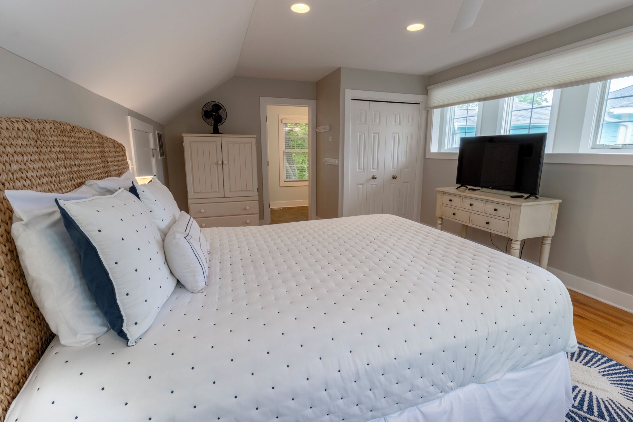 Un dormitorio con una cama grande, un televisor en una cómoda, un armario y una puerta que da a otra habitación.