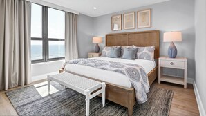 Een moderne slaapkamer met een groot bed, twee nachtkastjes, een bankje en uitzicht op zee.