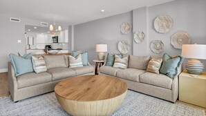 Een moderne woonkamer met een beigekleurige zithoek, een houten salontafel en decoratieve wandkunst.