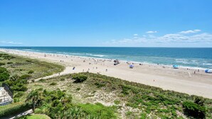 Een strand met een zandkust, een pier die het water in reikt, en enkele parasols en badgasten.