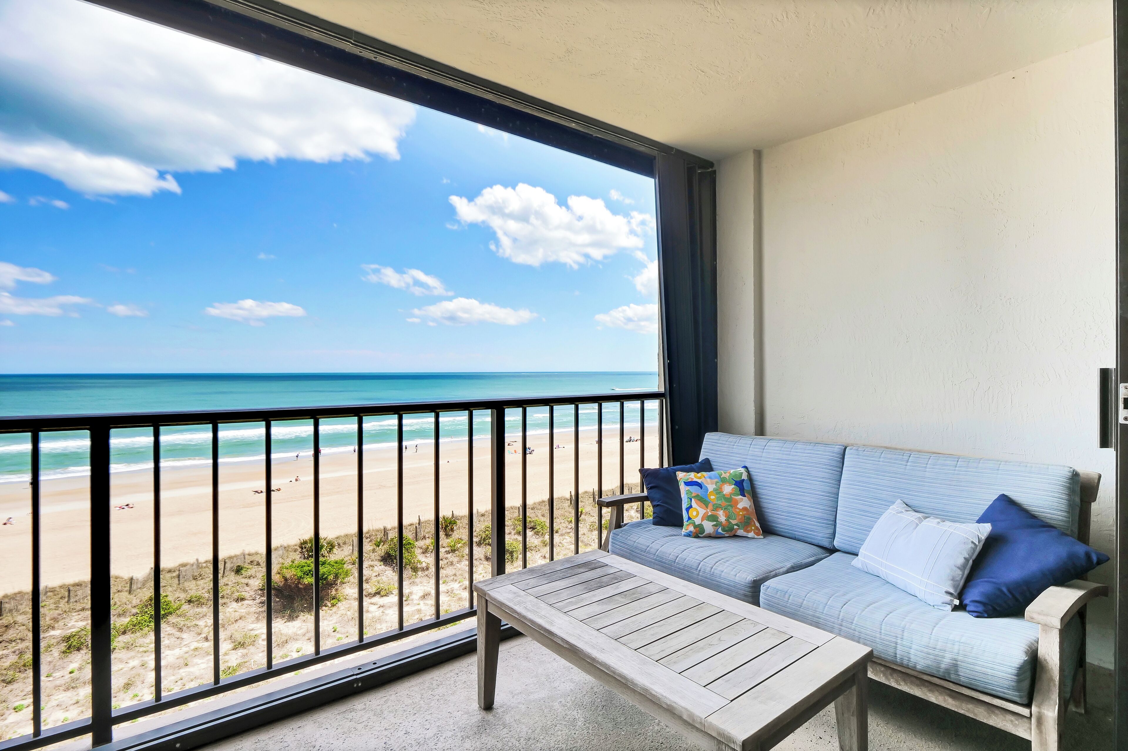Ein Balkon mit Blick auf den Strand, eine Couch und ein kleiner Tisch.