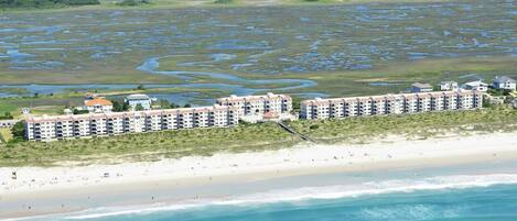 Un hôtel en bord de mer, composé de plusieurs bâtiments, avec une plage de sable et une zone marécageuse en arrière-plan.