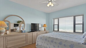 A bedroom with a bed, a TV, a dresser, a mirror, and a window with blinds. - DR 1405 - Beautiful oceanfront condo with tennis, pool and easy beach access (Wrightsville Beach)