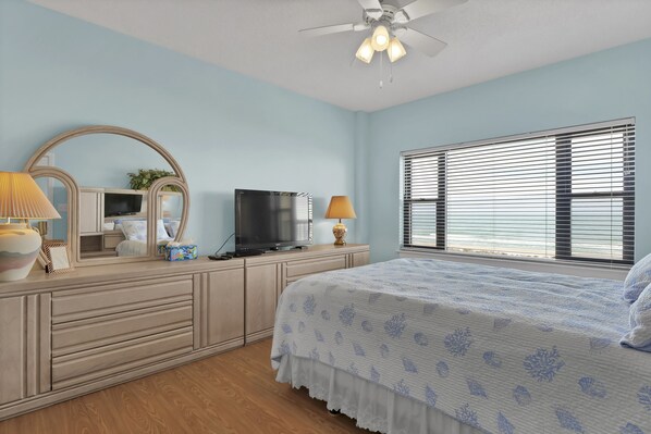 A bedroom with a bed, a TV, a dresser, a mirror, and a window with blinds. - DR 1405 - Beautiful oceanfront condo with tennis, pool and easy beach access (Wrightsville Beach)