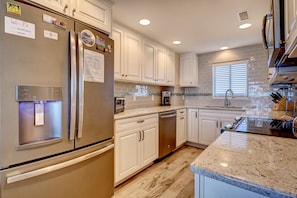 A modern kitchen with white cabinetry, stainless steel appliances, and a granite countertop. - Station One - 7I Seventh Heaven - Oceanfront condo community pool, tennis (Wrightsville Beach)