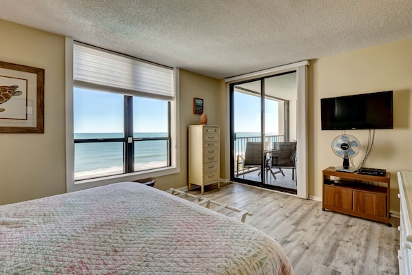A bedroom with a large bed, a dresser, a TV, and a balcony with a view of the ocean. - Station One - 7I Seventh Heaven - Oceanfront condo community pool, tennis (Wrightsville Beach)