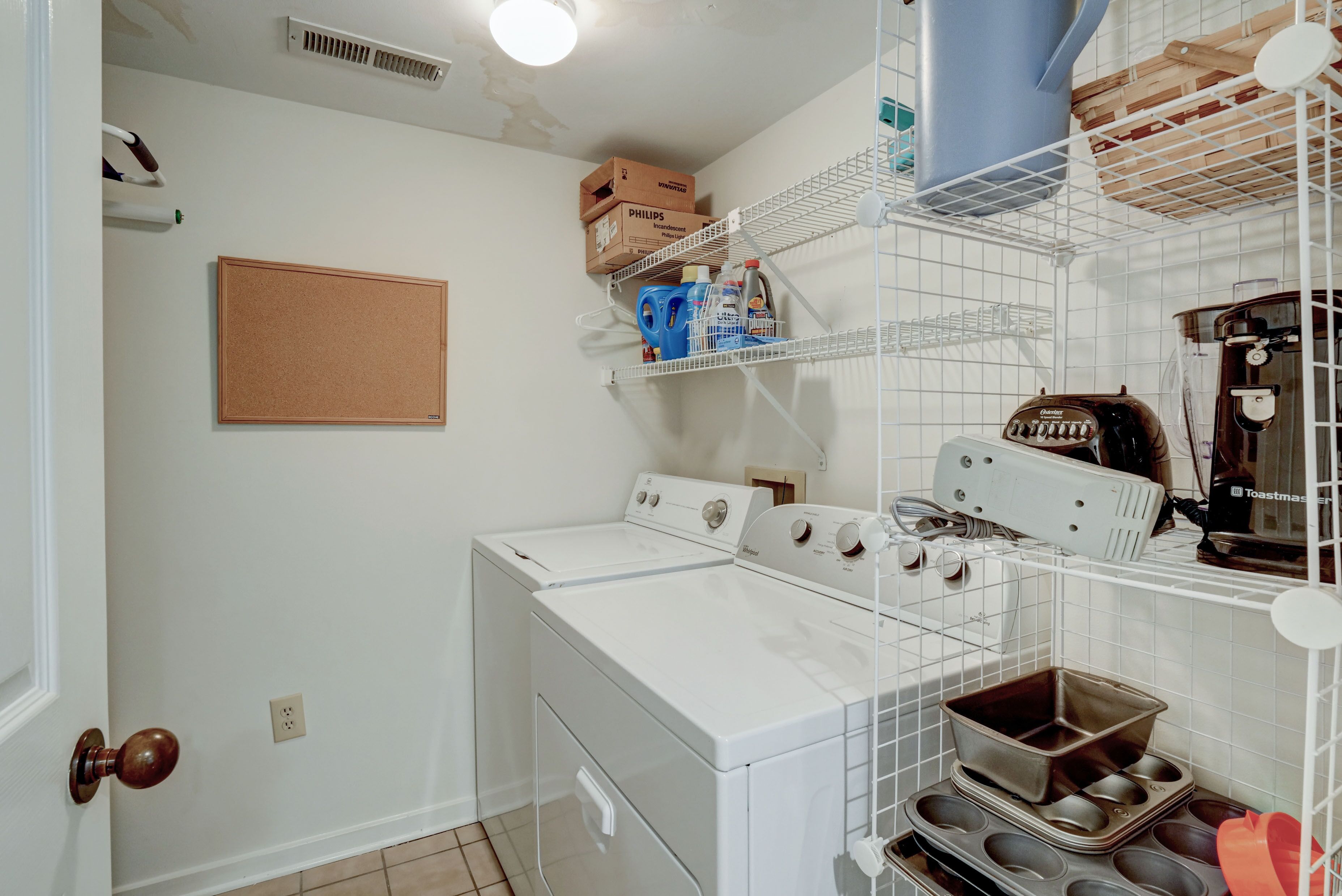 A laundry area with two white washers and dryers, shelves with boxes and bottles, and a toaster.