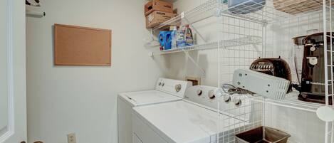 A laundry area with two white washers and dryers, shelves with boxes and bottles, and a toaster.