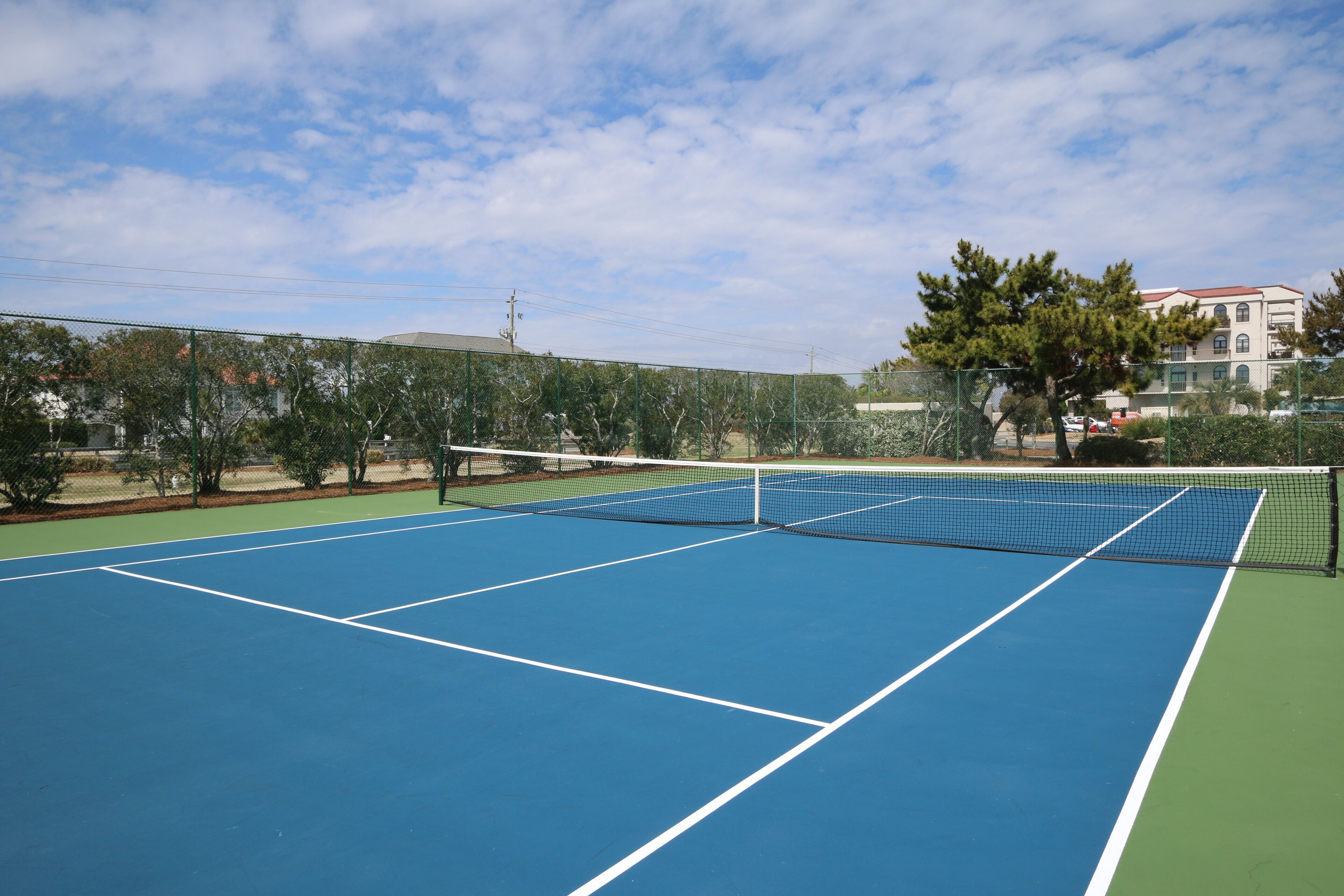 Un court de tennis avec un filet, entouré d’une clôture et d’arbres.